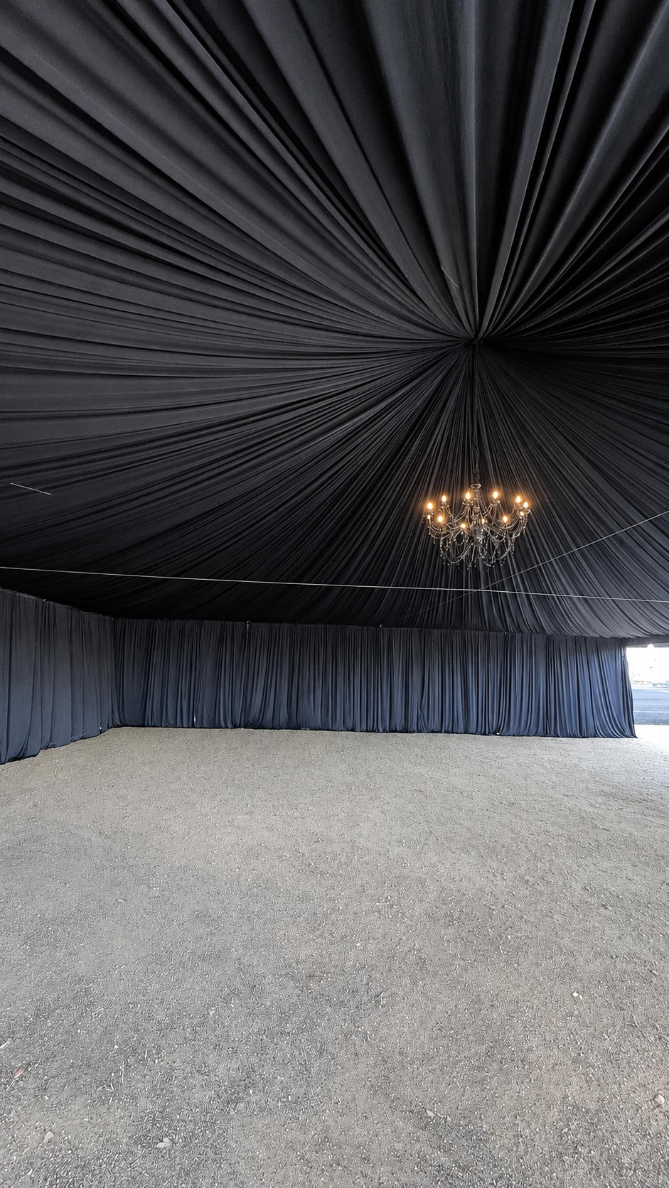 Actual AJ's Party Rentals installation with black ceiling draping, enclosed draped walls, and a chandelier